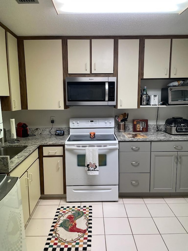 kitchen featuring white electric range oven, a toaster, light tile patterned floors, stainless steel microwave, and gray cabinetry