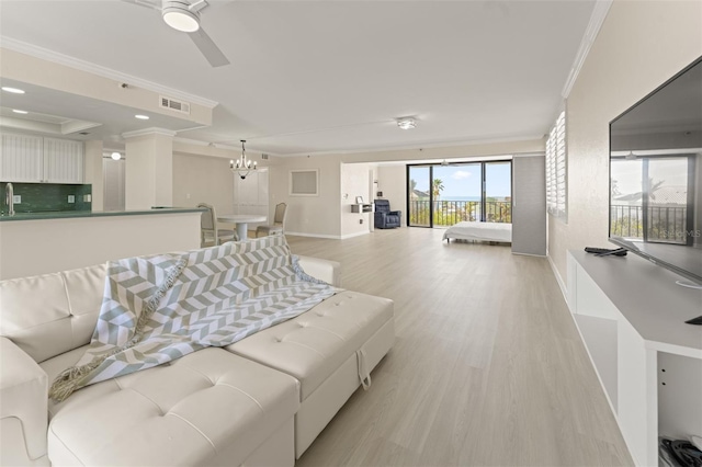 living area with visible vents, light wood-style floors, ornamental molding, baseboards, and ceiling fan with notable chandelier