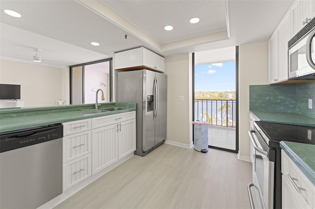 kitchen with stainless steel appliances, white cabinetry, a sink, and light wood finished floors