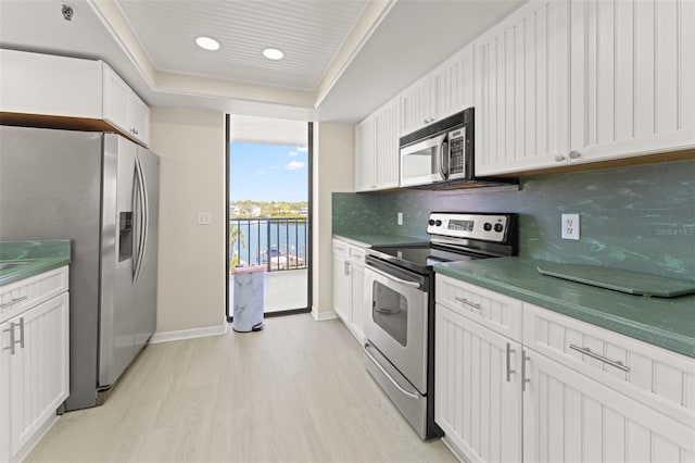 kitchen featuring stainless steel appliances, white cabinets, light wood finished floors, a raised ceiling, and tasteful backsplash