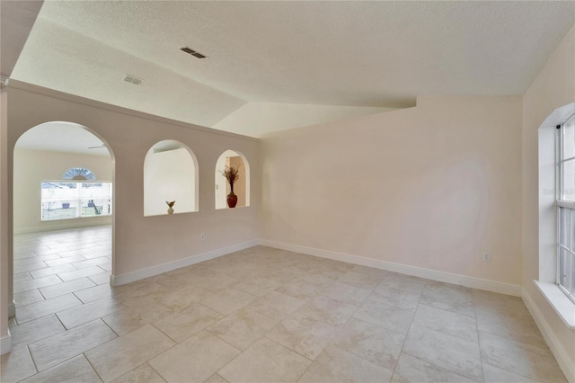 unfurnished room with a textured ceiling, arched walkways, visible vents, baseboards, and vaulted ceiling