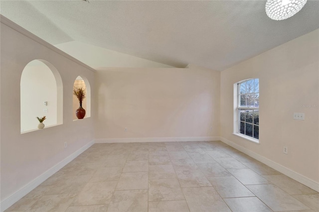 spare room featuring vaulted ceiling, a textured ceiling, and baseboards