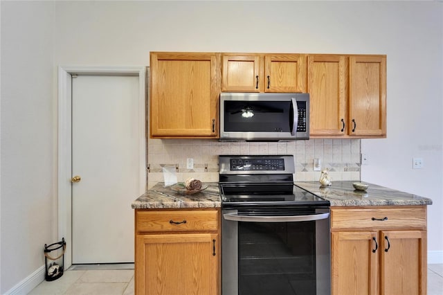 kitchen featuring light tile patterned floors, tasteful backsplash, appliances with stainless steel finishes, stone countertops, and baseboards