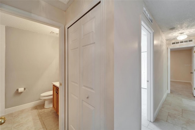 bathroom featuring a textured ceiling, toilet, visible vents, baseboards, and a closet