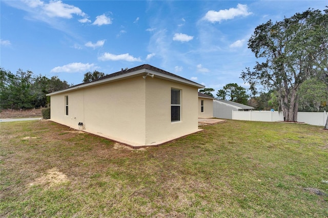 view of side of home featuring fence, a lawn, and stucco siding