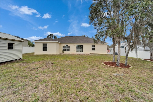 back of house with an outbuilding, stucco siding, fence, and a lawn