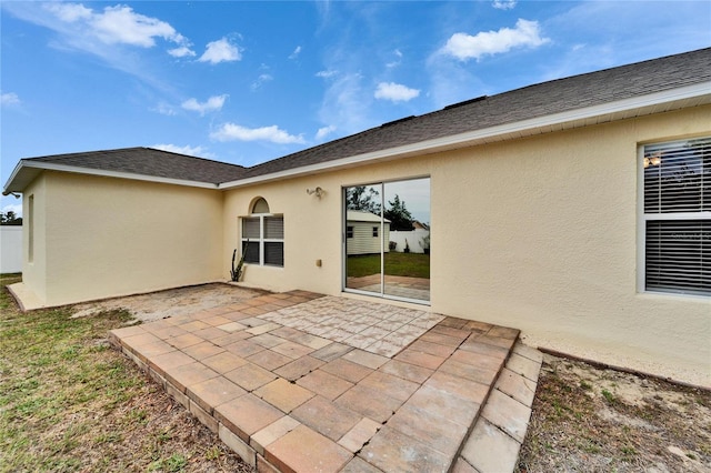 rear view of house featuring a shingled roof, a patio area, and stucco siding