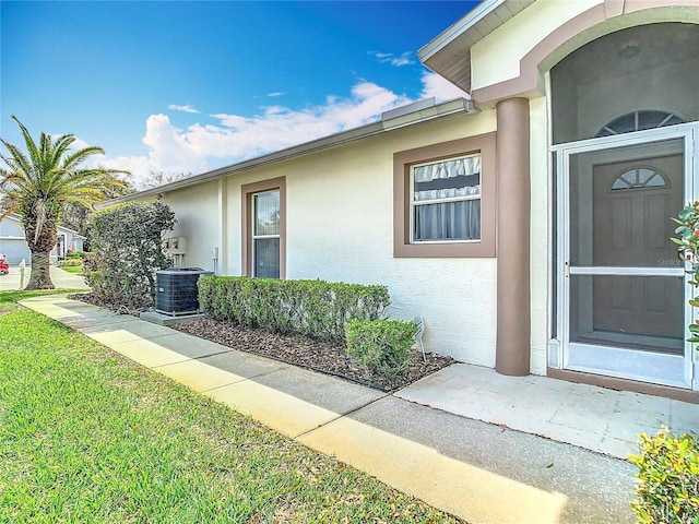 view of exterior entry with stucco siding, a lawn, and central AC unit