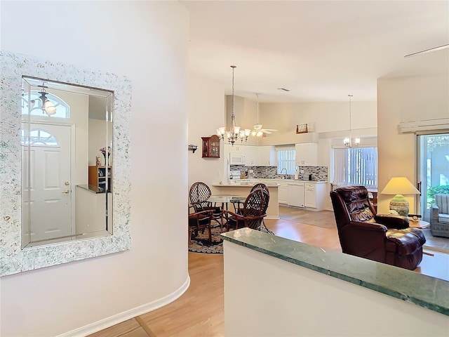 living area with baseboards, lofted ceiling, a chandelier, and light wood finished floors