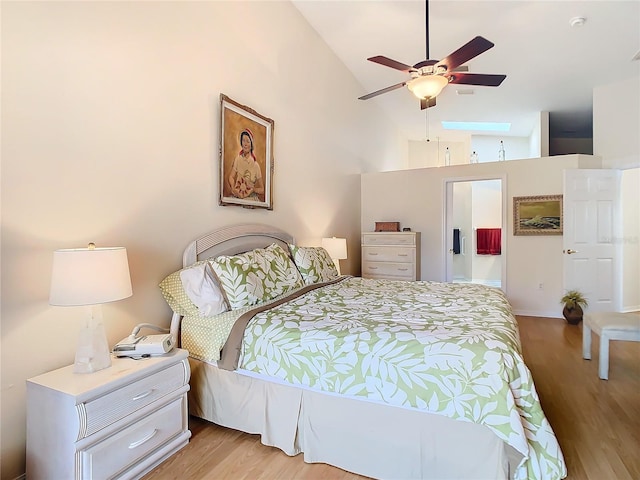 bedroom featuring high vaulted ceiling, a skylight, ensuite bathroom, and light wood-style floors