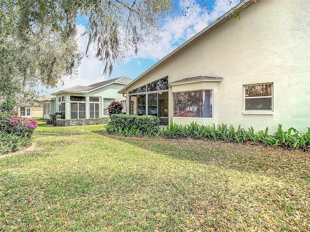 rear view of house with stucco siding, a yard, and a sunroom