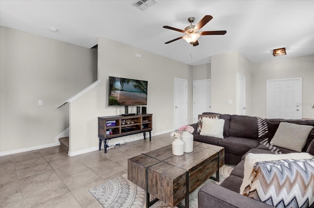 living room featuring visible vents, light tile patterned floors, baseboards, stairs, and ceiling fan