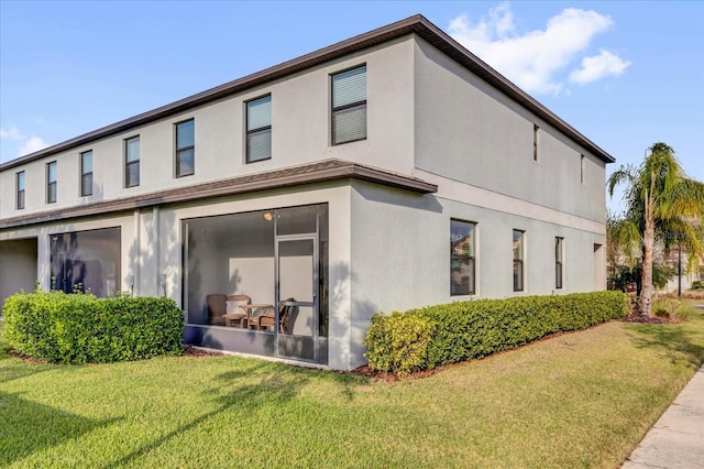rear view of property featuring a lawn and stucco siding