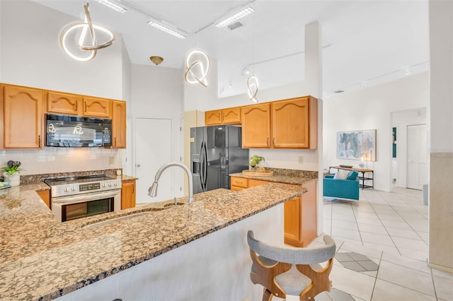 kitchen featuring light stone counters, light tile patterned floors, a towering ceiling, a sink, and black appliances