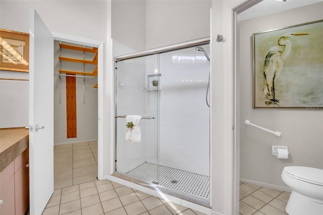 full bathroom featuring a walk in closet, toilet, a shower stall, tile patterned flooring, and baseboards