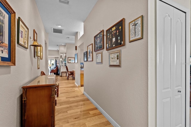 hallway with light wood-style floors, baseboards, and visible vents