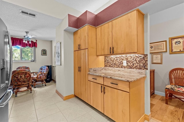 kitchen with light stone counters, stainless steel refrigerator with ice dispenser, tasteful backsplash, visible vents, and a textured ceiling