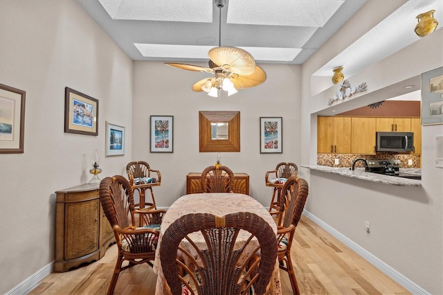 dining area with a skylight, light wood-style flooring, and baseboards