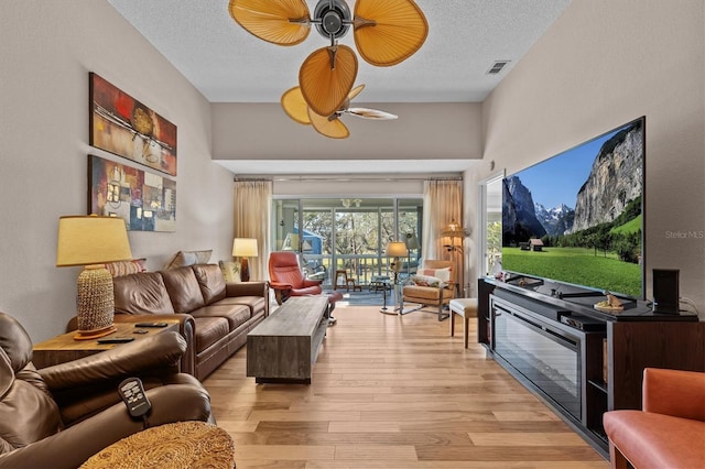 living room with light wood-style floors, visible vents, ceiling fan, and a textured ceiling