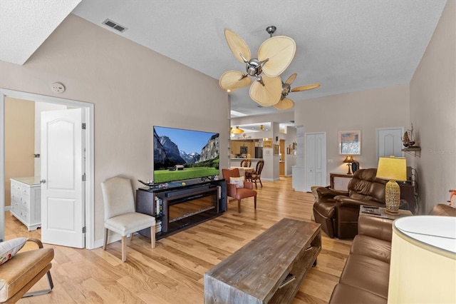 living area featuring visible vents, ceiling fan, a textured ceiling, light wood-type flooring, and baseboards