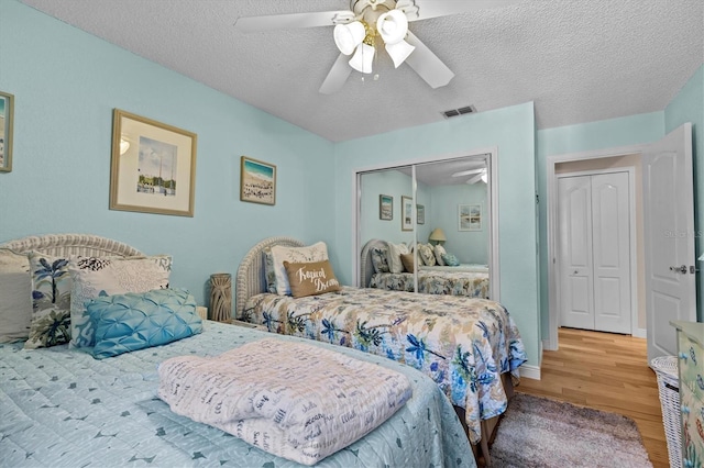 bedroom featuring a closet, visible vents, a ceiling fan, a textured ceiling, and wood finished floors