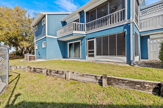 back of property with a yard, stucco siding, a sunroom, central AC, and a balcony