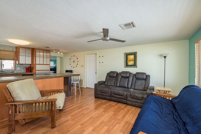 living area with light wood finished floors, ceiling fan, visible vents, and a textured ceiling