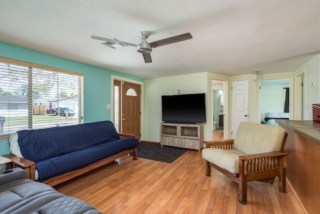 living room with visible vents, ceiling fan, light wood-style flooring, and a textured ceiling