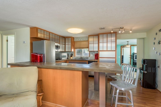 kitchen featuring stainless steel appliances, a peninsula, a sink, light wood finished floors, and tasteful backsplash