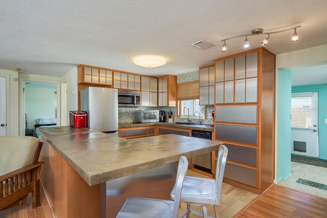 kitchen with light wood finished floors, stainless steel microwave, visible vents, freestanding refrigerator, and dishwashing machine