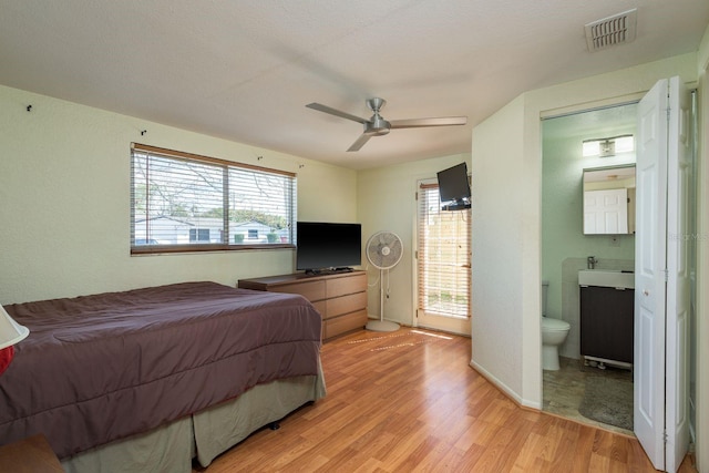 bedroom featuring light wood finished floors, visible vents, a sink, ceiling fan, and ensuite bath