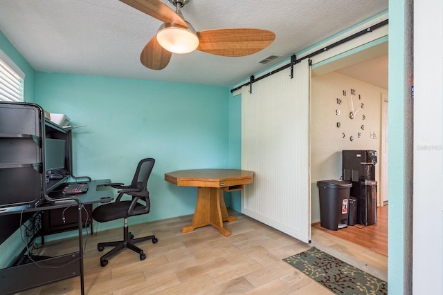 office space featuring visible vents, a barn door, ceiling fan, a textured ceiling, and wood finished floors