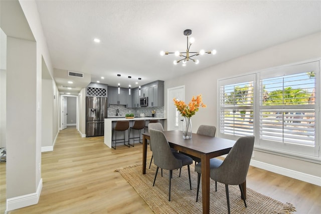dining room with light wood-type flooring, baseboards, and an inviting chandelier