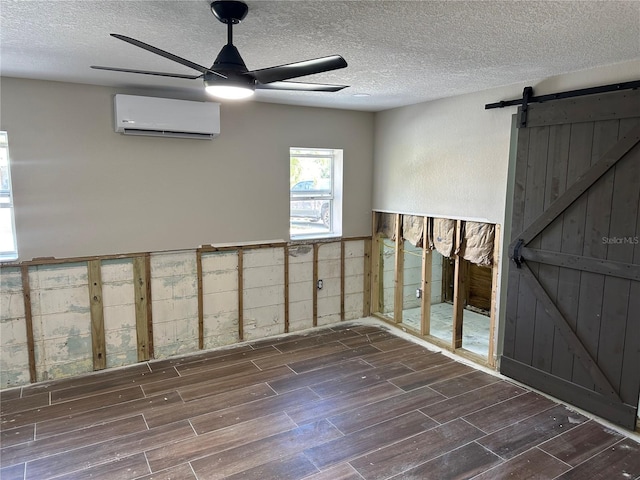 spare room with wood finish floors, a wall unit AC, a barn door, a ceiling fan, and a textured ceiling