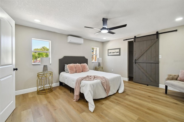 bedroom featuring multiple windows, a barn door, a wall mounted AC, and light wood-style flooring