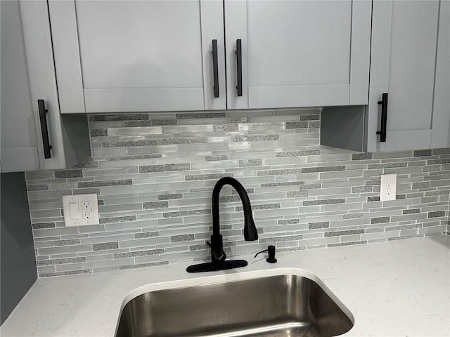 room details with light stone countertops, decorative backsplash, and a sink