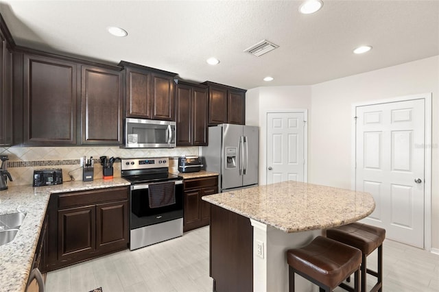 kitchen with tasteful backsplash, visible vents, a breakfast bar area, stainless steel appliances, and dark brown cabinets