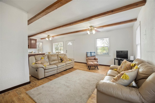 living area with ceiling fan, light wood-type flooring, beam ceiling, and baseboards