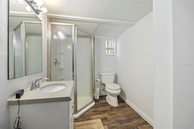 bathroom with wood finished floors, toilet, vanity, a textured ceiling, and a shower stall