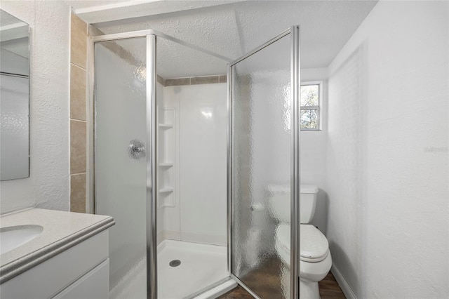 full bathroom featuring a textured wall, toilet, vanity, baseboards, and a shower stall