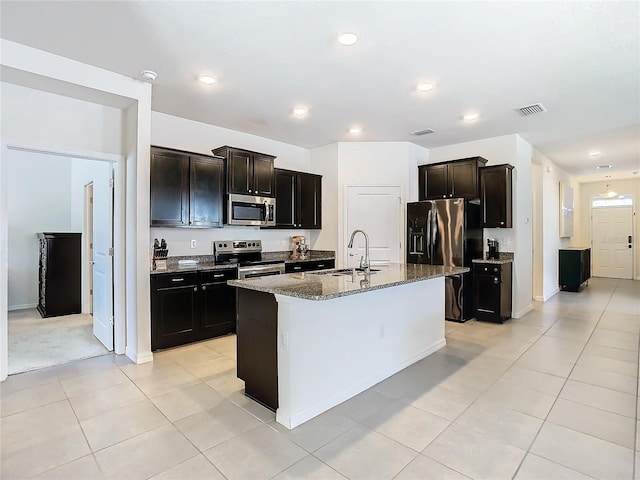 kitchen featuring visible vents, appliances with stainless steel finishes, a sink, an island with sink, and dark stone countertops