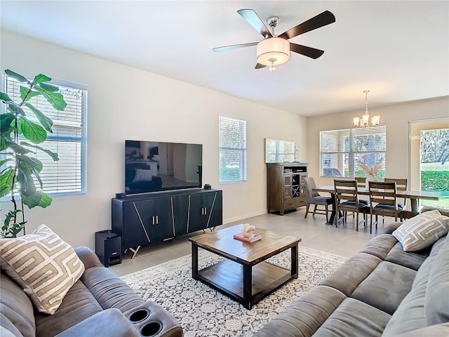 living area featuring ceiling fan with notable chandelier, light tile patterned floors, plenty of natural light, and baseboards