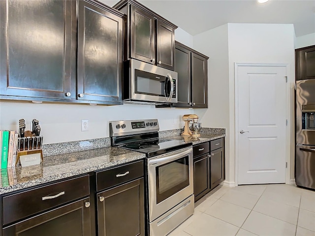 kitchen with light tile patterned floors, stainless steel appliances, dark stone countertops, and dark brown cabinetry