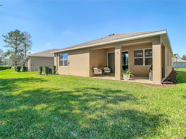 rear view of house featuring a patio area, a lawn, and stucco siding