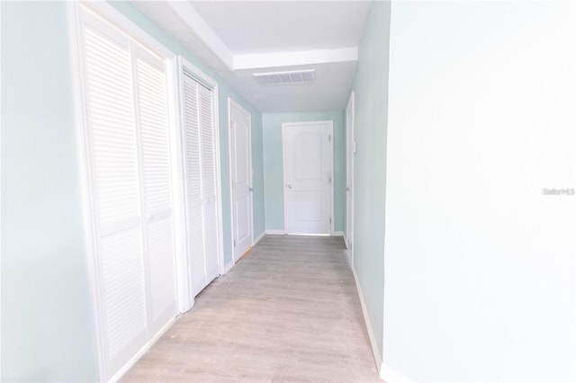 hall with light wood-type flooring, visible vents, and baseboards