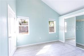 unfurnished bedroom with high vaulted ceiling, baseboards, and a closet