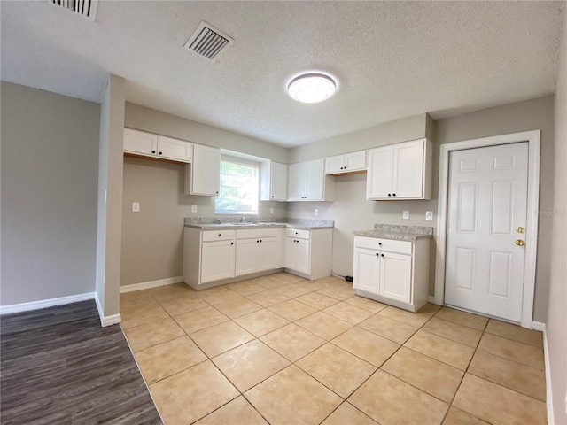 kitchen featuring a sink, visible vents, baseboards, white cabinetry, and light countertops