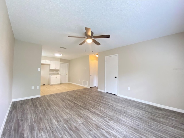 unfurnished living room with a textured ceiling, light wood-type flooring, visible vents, and baseboards