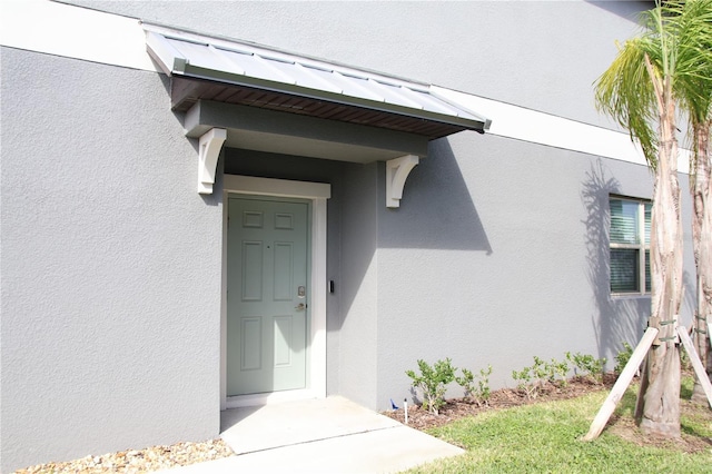 entrance to property featuring a standing seam roof, metal roof, and stucco siding