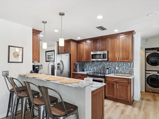 kitchen featuring appliances with stainless steel finishes, stacked washer and dryer, a kitchen bar, and tasteful backsplash